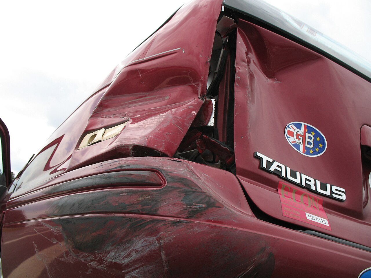 Close-up of a red car with a crumpled rear side panel and damaged door after a collision.