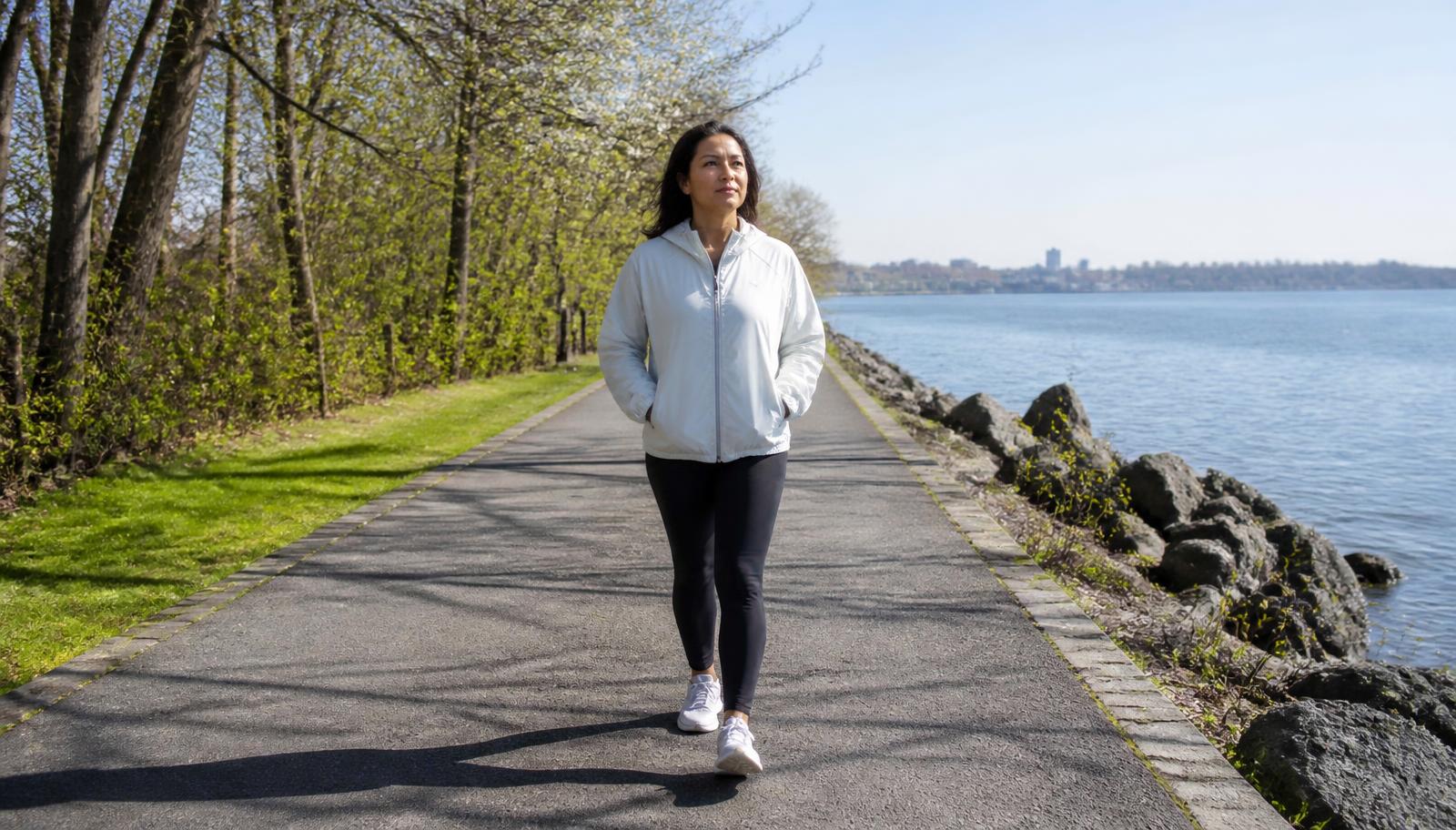An adult walking confidently along a bright riverside path on a clear morning