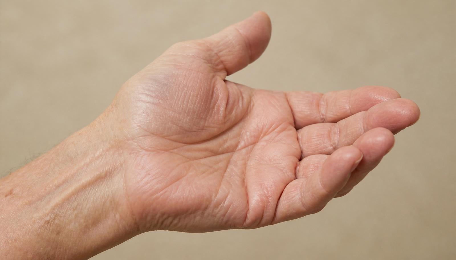 Close-up of an older adult's open hand resting palm upwards against a plain warm background